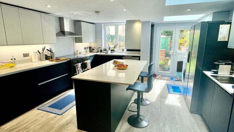 The finished open-plan kitchen, with a stone-topped breakfast bar, dark handleless units, a large skylight and doors onto the garden