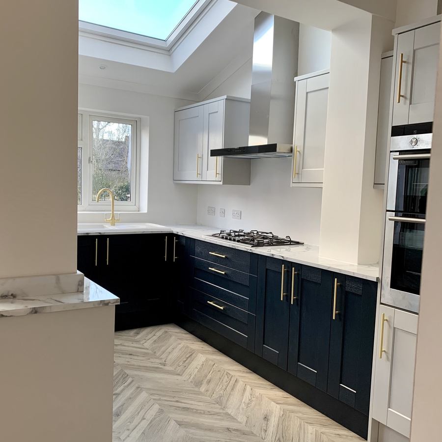 Navy shaker kitchen with brass handles, integrated ovens and herringbone flooring